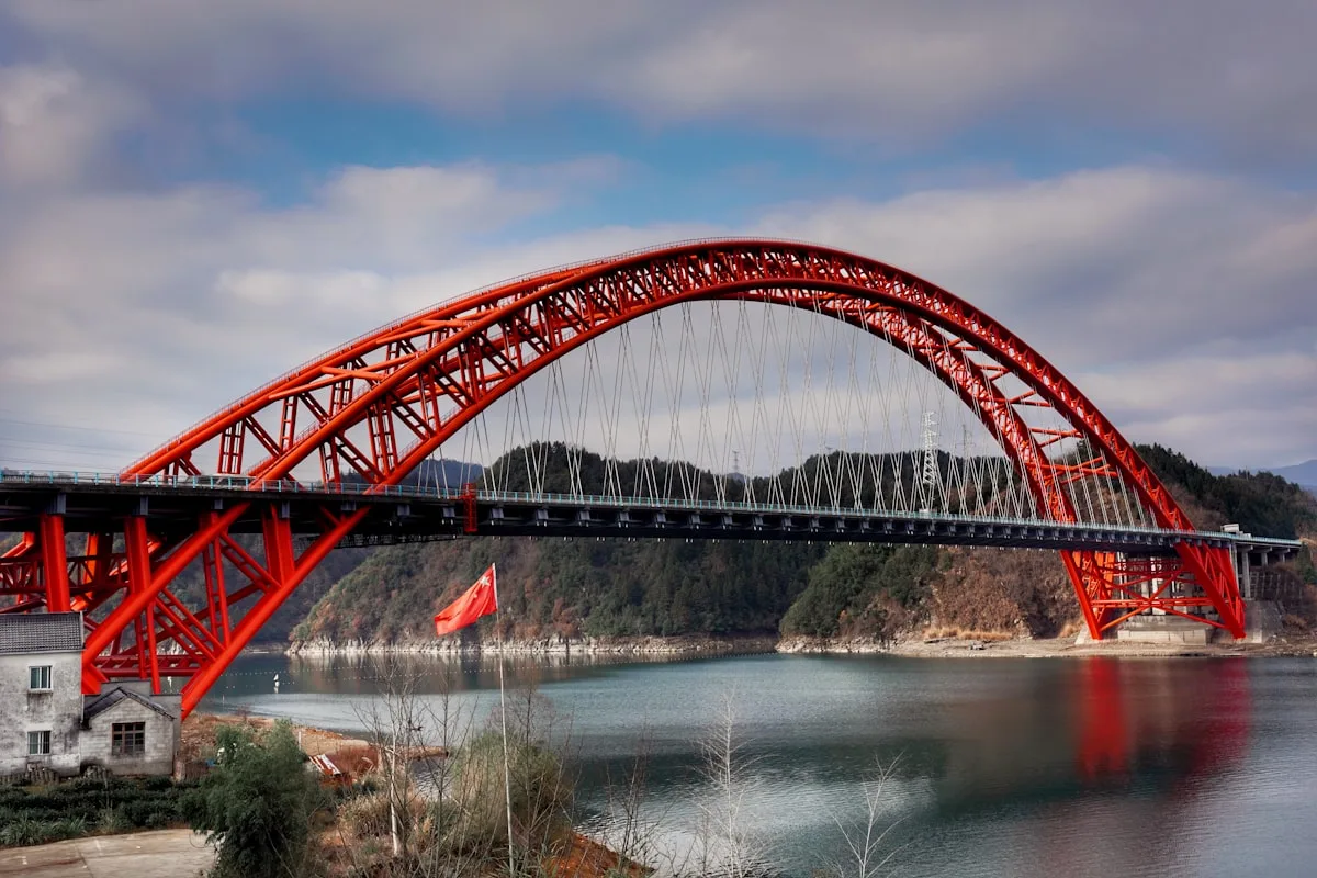 pont métallique rouge au-dessus d'une rivière sous un ciel nuageux en journée