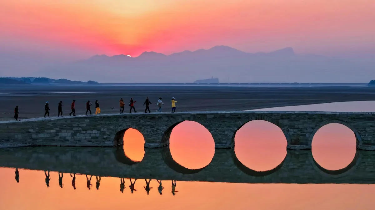 Des personnes traversent un pont aux ouvertures circulaires au coucher du soleil.