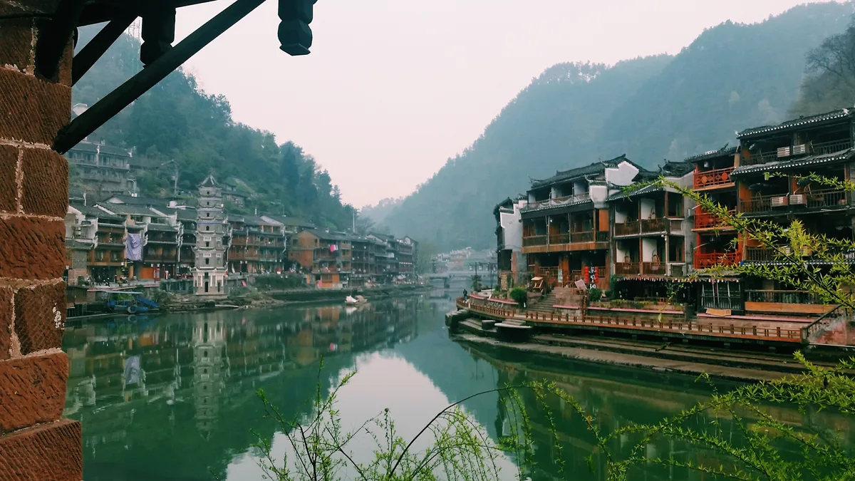 Bruma matinal sobre el Tuojiang en Fenghuang, con los tejados del pueblo y una pagoda en la orilla opuesta reflejados en el agua quieta (Foto: Yunzhongjun vía Wikimedia Commons)