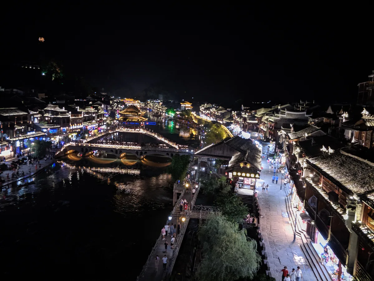 Fenghuang de noche vista desde arriba, con el puente Hongqiao iluminado cruzando el Tuojiang y la gente en los paseos junto al río (Foto: Sunyiming vía Wikimedia Commons)