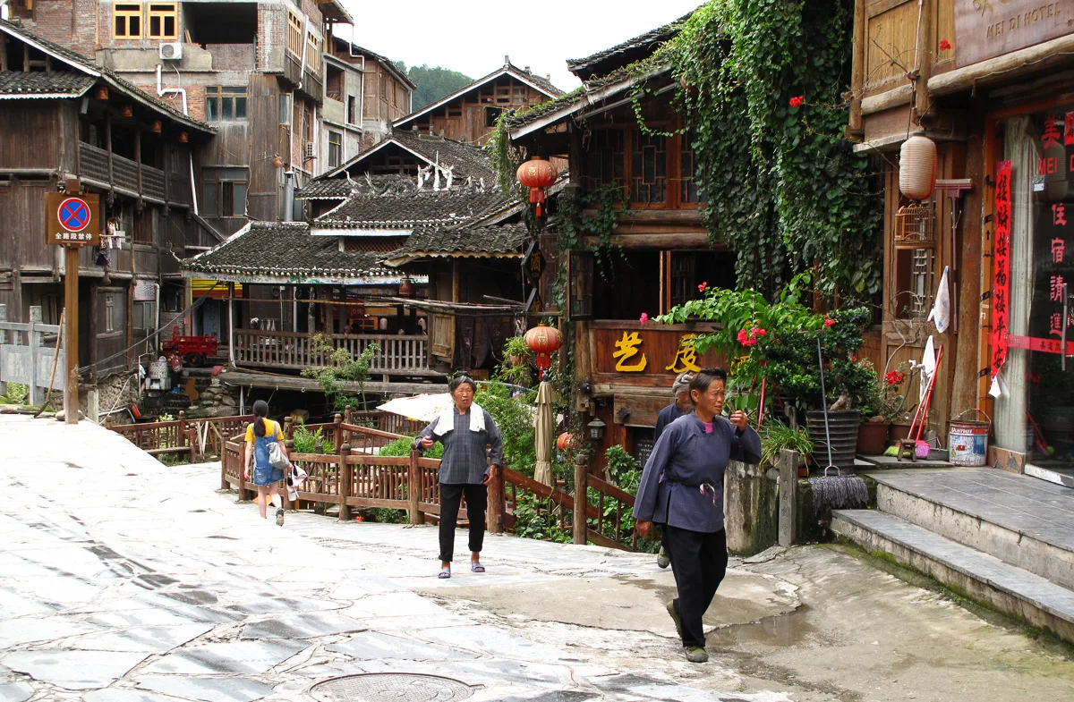 A stone-paved street in Zhaoxing with wooden stilt houses, residents and visitors sharing the lane (Photo: Rutger van der Maar via Wikimedia Commons)
