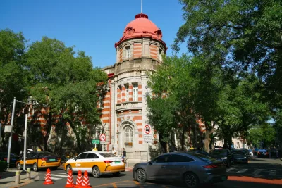 Beijing taxis in blue and yellow livery passing a red-domed historic building on a tree-lined street