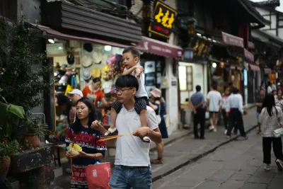 Man carries child on shoulders walking down a crowded street
