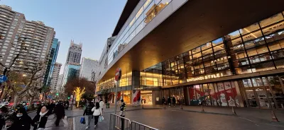 The glass frontage of Xintiandi Style I in Shanghai at dusk, with shoppers walking past on the pavement and apartment towers behind (Photo: Juan Antonio Segal via Wikimedia Commons)