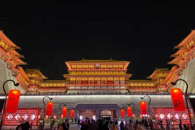 La tour-porte illuminée de Yingtianmen à Luoyang la nuit, un toit Tang à trois niveaux dans une lumière dorée au-dessus d'un soubassement de pierre, avec la foule et des lanternes rouges au premier plan (Photo: Windmemories via Wikimedia Commons)