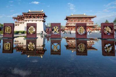 L'esplanade d'entrée du parc Tang Paradise à Xi'an, cinq stèles de pierre portant les caractères du nom reflétés dans un bassin, avec des pavillons Tang à toits dorés et des visiteurs en hanfu (Photo: xiquinhosilva via Wikimedia Commons)
