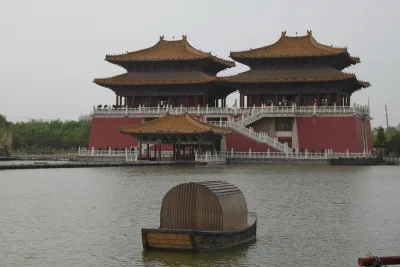 Deux pavillons de style Song aux toits dorés et aux balustrades de pierre blanche posés sur un lac au jardin Qingming Shanghe à Kaifeng, avec une barque en bois au premier plan (Photo: Gary Todd via Wikimedia Commons)
