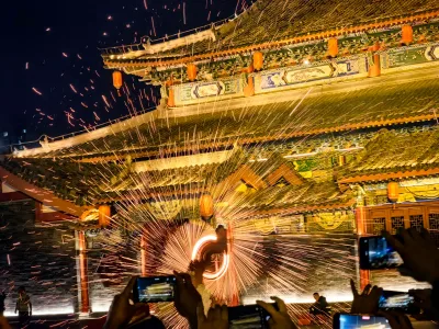 De la fonte en fusion projetée contre la façade sculptée d'un temple chinois la nuit, pendant un spectacle de fleur de fer, avec le public qui filme au téléphone (Photo: Auongkinghe via Wikimedia Commons)