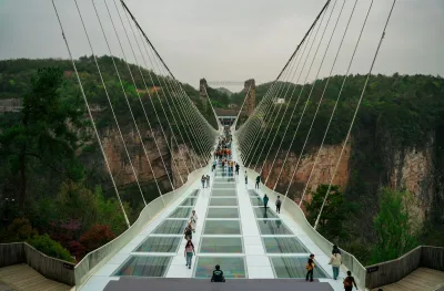 Visitors walking across the transparent deck of the cable-stayed glass bridge at Zhangjiajie Grand Canyon, canyon walls and forest on both sides
